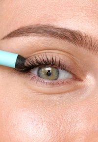 Una matita per eyeliner nera viene applicata su una palpebra di colore chiaro. La pelle è liscia e l'occhio presenta una miscela di tonalità verdi e grigie.