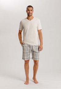 Camisa de cuello en V de color crema, ligera y de manga corta, combinada con pantalones cortos a cuadros en tonos azul claro, beige y gris. Tejido suave, corte casual.