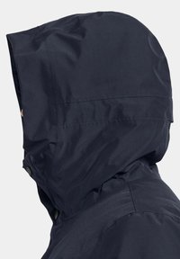 Marinblå huva-jacka med ett slätt, vattenavvisande material. Har en dragsko på huvan och synliga sömnadsdetaljer. Knapplåsning vid nacken.