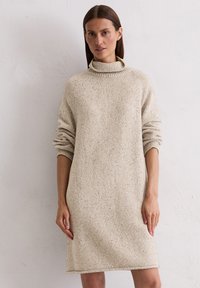 Beige Strickkleid mit hohem Kragen, langen Ärmeln und lockerer Passform. Texturiertes Muster mit kleinen Sprenkeln durchzogen.