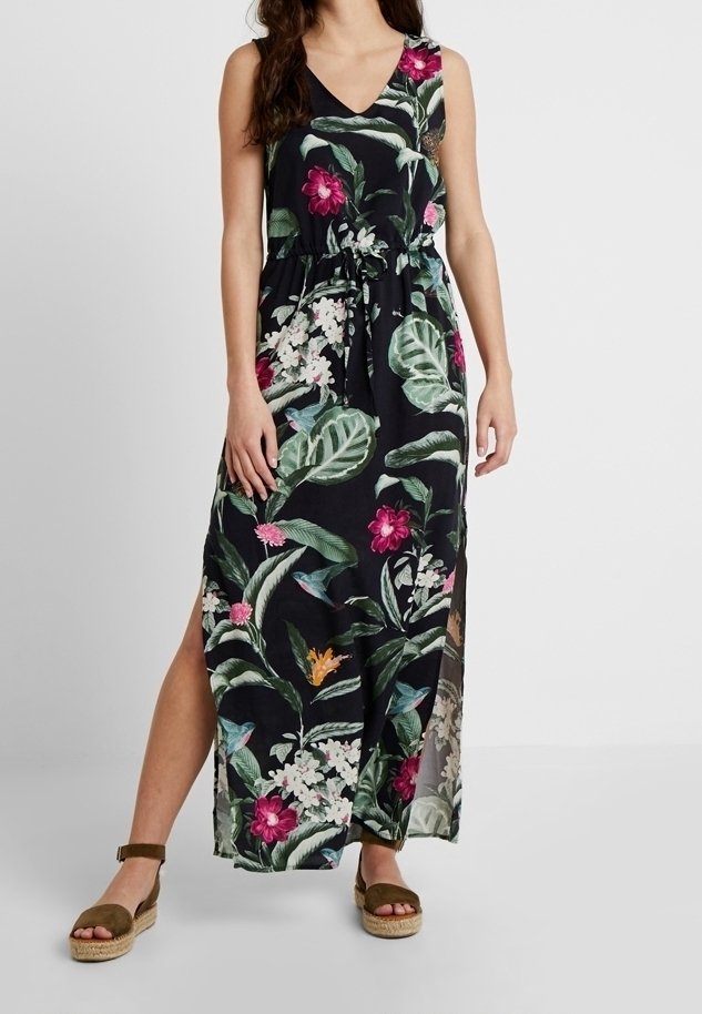 Vestido largo negro con patrones florales vibrantes, con escote en V, cinturón ajustable y aberturas laterales. Combinado con sandalias de esparto.