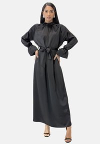 Zwarte satijnen jurk met lange mouwen, hoge hals, taille met ceintuur, geplooide mouwen en een vloeiende silhouet. Gladde textuur en minimalistisch ontwerp.