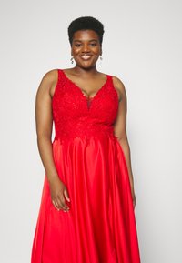 Rotes Abendkleid mit tiefem V-Ausschnitt, verziertem Oberteil und fließendem Satinrock, der florale Muster und Perlenakzente aufweist.