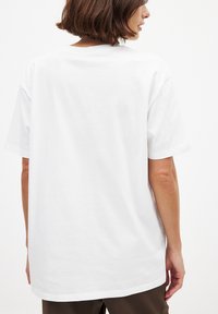 Hvid bomulds t-shirt med korte ærmer, rund halsudskæring og en afslappet pasform. Stoffet ser glat ud med en ensartet tekstur og ingen synlige mønstre.