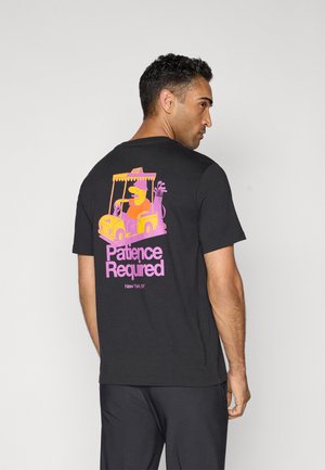 Black cotton T-shirt featuring a vibrant graphic of a character in a yellow taxi with the text "Patience Required" in pink.