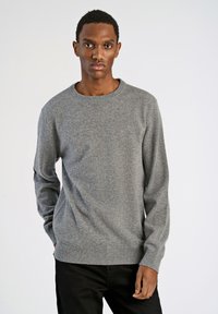 Grauer Strickpullover mit Rundhalsausschnitt, langen Ärmeln sowie gerippten Bündchen und Saum, getragen von einer Person vor einem einfarbigen Hintergrund.