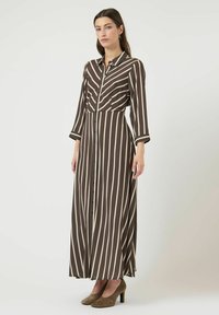 Robe longue à rayures marron et crème avec un devant à boutons, un col à revers et des manches longues. Portée avec des escarpins en daim vert.