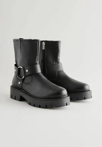 Mustad nahast ankle saapad külgzippers, tugeva kummitald ja dekoratiivne rihm, millel on ümmargune metallne klamber.
