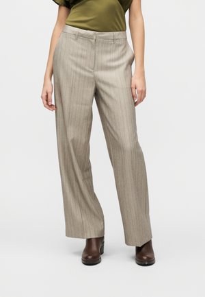 Pantaloni a righe beige con vestibilità ampia, caratterizzati da una parte frontale piatta e tasche laterali. Il tessuto ha una texture morbida. Abbinati a stivaletti marrone scuro.