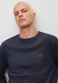 Marineblauwe sweatshirt met een ronde hals, voorzien van een klein reliëflogo-tag op de borst, gemaakt van zachte, textuurstof.