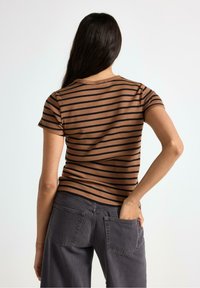 Brun og sort stribet ribbet t-shirt med korte ærmer, tætsiddende design og rund halsudskæring, parret med mørkegrå bukser med baglommer.