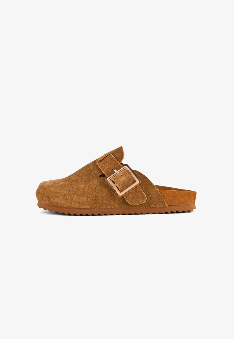 Zapato de ante marrón, tipo slip-on, con una amplia correa y detalle de hebilla, que presenta una plantilla contorneada y una suela de goma texturizada.