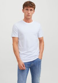T-shirt en coton blanc avec un col rond et des manches courtes. Texture lisse, coupe décontractée. Associé avec un jean bleu clair. Pas de motifs ni d'accents.