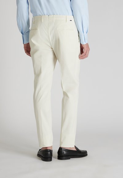 Pantaloni bianchi in cotone con vestibilità slim, due tasche posteriori e passanti per cintura, abbinati a mocassini neri. Sfondo grigio chiaro.