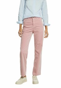 Personne portant une chemise bleu clair à manches longues, un pantalon rose droit et des baskets blanches, debout, bras détendus le long du corps.