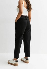 Czarne, zwężane spodnie z talią i bocznymi kieszeniami, zestawione z białymi i brązowymi tenisówkami. Stylizacja zawiera prosty, biały top na ramionach.