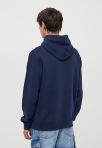 Granatowy hoodie wykonany z miękkiego materiału, z kapturem na sznurku, ribbowanymi mankietami i dołem, o luźnym kroju i bez widocznych grafik.