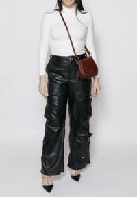 Pantaloni cargo in pelle nera con molte tasche, vita alta e gambari larghi. Abbinate a un top aderente bianco a maniche lunghe e una borsa a tracolla marrone.