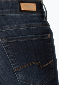 Donkerdenim jeans met een vierkante patch met reliëfmerklogo, koperen klinknagels en gouden stiksels op het ontwerp van de achterzak.