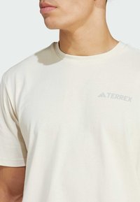 Kremasta Terrex majica od mekog materijala s okruglim izrezom i kratkim rukavima, s diskretnim sivim logom na prsima.