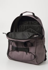 Purple fabric backpack with a padded, black interior. Features adjustable straps, a buckle closure, and exterior mesh pockets.
