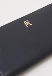 Námořnická kožená peněženka s výrazným zlatým logem, hladkým povrchem a elegantním designem s viditelným švem.