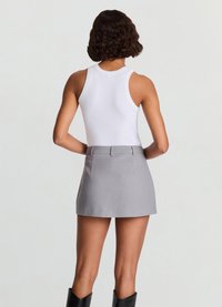 Ribbed white tank top paired with a gray mini skirt. The skirt has a smooth texture and a tailored design, featuring back pockets and belt loops.