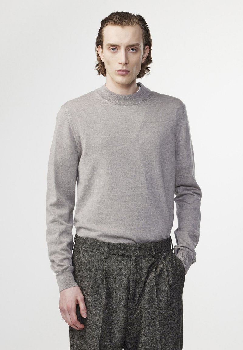 Light gray knit sweater with a high rounded neckline, long sleeves, and a soft texture, paired with dark gray pleated trousers.