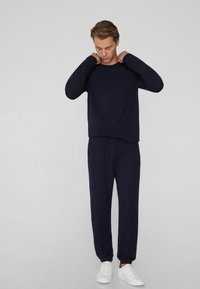 Marineblauw shirt met lange mouwen en bijpassende broek gemaakt van een zachte stof. De broek heeft een elastische tailleband met een trekkoord. Witte sneakers inbegrepen.