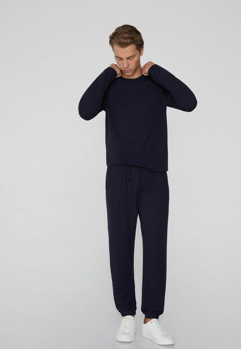 Marineblauw shirt met lange mouwen en bijpassende broek gemaakt van een zachte stof. De broek heeft een elastische tailleband met een trekkoord. Witte sneakers inbegrepen.