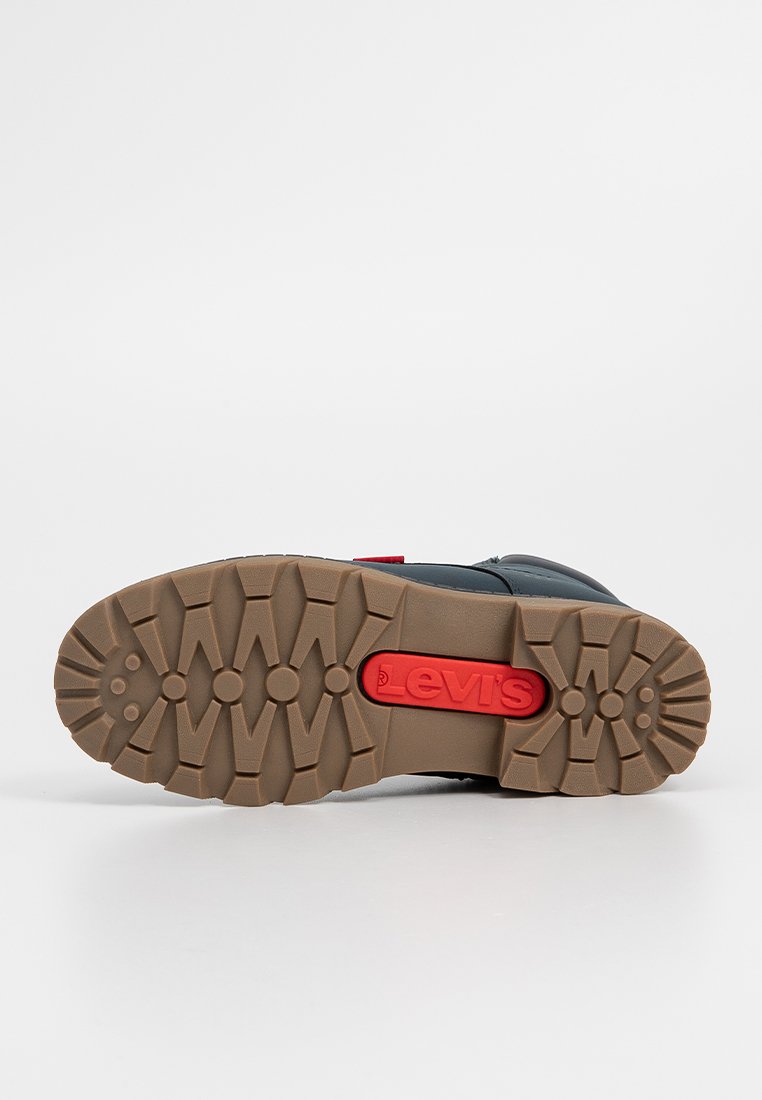 Levi's schoeisel met een dikke, getextureerde bruine rubberen zool met een rood logo-accent. Het bovenste deel is donkerblauw met zwarte details.