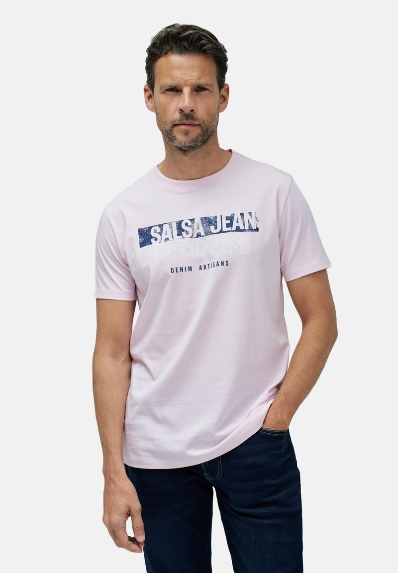 Světle růžové tričko s krátkým rukávem, na kterém je modrý potisk "Salsa Jean Denim Artisans", kulatý výstřih a jemná textura tkaniny.