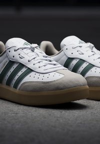 Weiße Sneakers mit grünen Streifen, Wildleder-Zehenkappe und perforiertem Design. Die Sohle aus Gummi sorgt für Traktion und Komfort. Mit Schnürdesign.