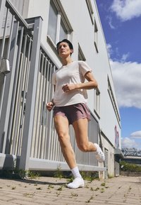 Runner in a light-colored, short-sleeved shirt and maroon shorts. White shoes and socks. Gray railing and building in background.