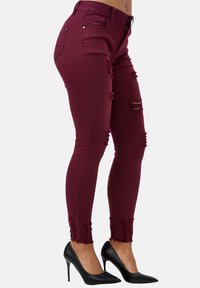Jeans skinny burdeos con detalles desgastados, dobladillo deshilachado y ajuste de cintura media, combinados con zapatos de tacón negros.