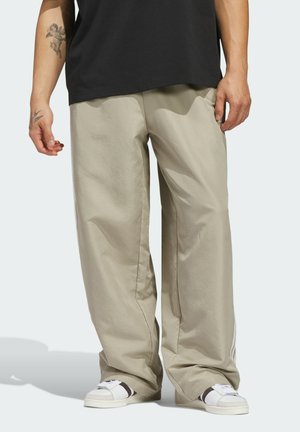 Laajah beige pants yang terbuat dari bahan ringan, memiliki tekstur halus dan potongan longgar. Dipadukan dengan sepatu sneakers putih dan atasan hitam.