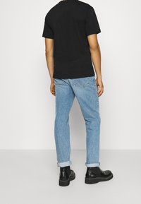 Camiseta negra de manga corta combinada con jeans de color azul claro. Los jeans están remangados en los puños, complementados con botas negras hasta el tobillo.