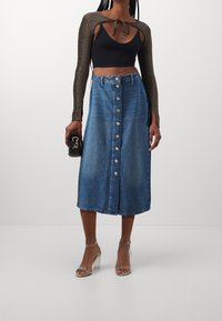 Černý crop top s dlouhými, třpytivými rukávy, spárovaný s midi modrou džínovou sukní s předním zapínáním na knoflíky a mírně A-liniovým střihem.