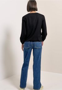 Maglietta nera a maniche lunghe con dettagli decorativi sui polsini, abbinata a jeans a zampa d'elefante blu e scarpe da ginnastica chiare.