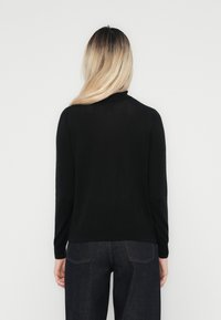 Pull noir à manches longues, col côtelé et texture lisse. Associé à un jean foncé, vu de dos sur un fond blanc.