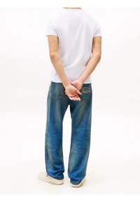 White short-sleeve t-shirt, relaxed-fit blue denim jeans with back pocket embroidery, and light-colored sneakers. Clear, minimal style.