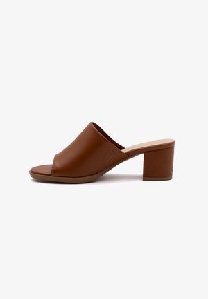 Mules ouvertes en cuir marron avec une texture lisse, présentant un design courbé et un talon bloc de hauteur moyenne avec des détails en relief.