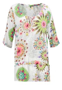 Blouse tunique blanche avec des motifs floraux et géométriques colorés, manches trois-quarts et petit nœud à l'avant au niveau de l'encolure.