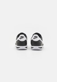 Sneakers Nike alb-negru au un brâu din piele netedă, guler captusit și o talpă exterioară albă în contrast cu un model de aderență.