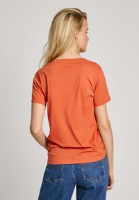 T-shirt �à manches courtes, col rond en coton corail, offrant une coupe décontractée et une texture lisse. Associé à un jean en denim bleu taille haute.