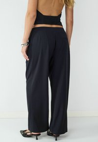 Czarne spodnie o szerokich nogawkach z subtelną fakturą, charakteryzujące się luźnym krojem, przeszywaną talią i bocznymi kieszeniami, zestawione z czarnymi szpilkami.