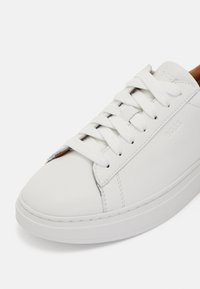 Hvide lædersneakers med flade hvide snører, rund tå, glat tekstur og minimalistisk design. 'BOSS' logoet præget på siden.