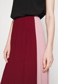 Jupe colorée en blocs rouge et rose avec une texture froissée, dotée d'une taille élastique, associée à un haut noir ample.