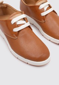 Chaussures en cuir perforé marron avec des lacets blancs et une semelle blanche contrastante. Design à bout rond avec une texture lisse et des détails de couture.