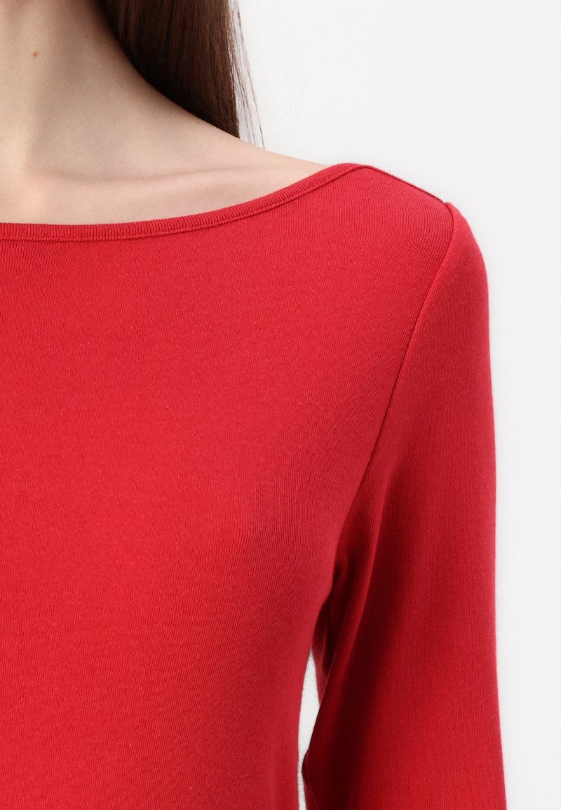 Haut rouge à manches longues avec un large col bateau. Fabriqué en tissu lisse et extensible, il présente un design ajusté et des finitions côtelées.